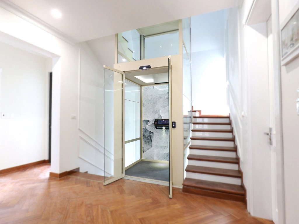 المصاعد المنزلية 1 Cibes V90 home lift installed beside a staircase inside a modern villa, featuring glass shaft and marble-patterned back panel.